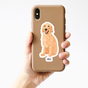 K&ouml;nnte beinhalten: Eine Handyh&uuml;lle mit einem Aufkleber eines sitzenden Golden Retrievers. Der Aufkleber tr&auml;gt den Namen "Mila".