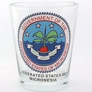 Puede incluir: Un vaso de chupito de vidrio transparente con un sello azul y rojo con las palabras "Government of the Federated States of Micronesia". El sello tiene una planta roja y verde con las palabras "Peace, Unity, Liberty" en una pancarta blanca.