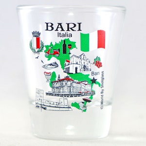 Pode incluir: Um copo de shot de vidro transparente com um design verde e branco da cidade de Bari, Itália. O design inclui um scooter, um barco, um edifício e a bandeira italiana. O texto "Bari Italia" está impresso no copo.