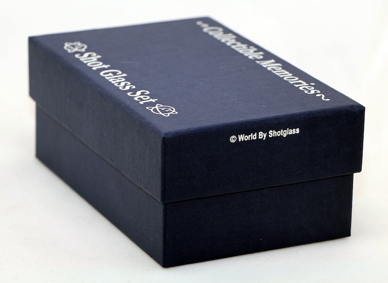May include: A navy blue box with the text "Shot Glass Set" and "Collectible Memories" printed in silver on the top. The bottom of the box has the text "World By Shotglass" printed in silver.