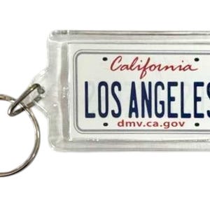 Pode incluir: Chaveiro retangular transparente com um design de placa de carro da Califórnia. A placa diz "LOS ANGELES" em letras azuis em negrito, com "California" em escrita vermelha acima. O site dmv.ca.gov está impresso na parte inferior.