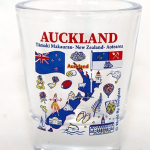 Peut inclure: Un verre à shot en verre transparent avec une illustration colorée de la région d'Auckland en Nouvelle-Zélande. L'illustration comprend le drapeau néo-zélandais, un kiwi et le texte "Auckland, Tamaki Makaurau - Nouvelle-Zélande - Aotearoa".