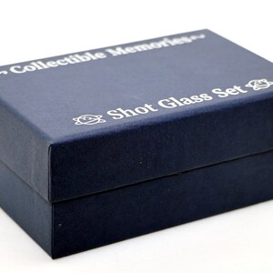 May include: A navy blue box with the text "~Collectible Memories~ Shot Glass Set" printed in white on the top. The box has a small, white, stylized atom symbol on the left and right sides of the text.