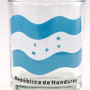 May include: A clear glass shot glass with the flag of Honduras printed on it. The flag is blue, white, and has five white stars. The text "República de Honduras" is printed on the bottom of the glass.