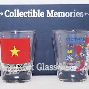 May include: Two clear glass shot glasses with a Vietnam theme. One glass features the Vietnamese flag with a red background and a yellow star. The other glass has a map of Vietnam with various landmarks and the text "VIETNAM" in blue.