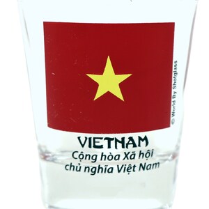 May include: A clear glass shot glass with a red and yellow Vietnamese flag design. The text "VIETNAM" is printed in black below the flag, and the text "Cộng h&ograve;a X&atilde; hội chủ nghĩa Việt Nam" is printed in black below the word "VIETNAM". The text "World By Shotglass" is printed in black on the right side of the glass.