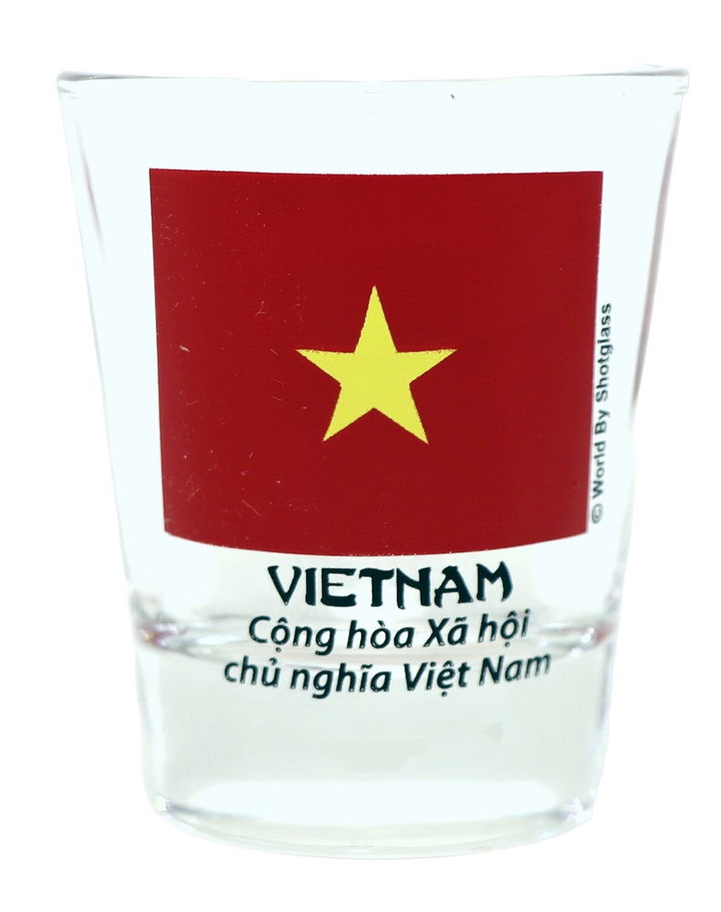 May include: A clear glass shot glass with a red and yellow Vietnamese flag design. The text "VIETNAM" is printed in black below the flag, and the text "Cộng h&ograve;a X&atilde; hội chủ nghĩa Việt Nam" is printed in black below the word "VIETNAM". The text "World By Shotglass" is printed in black on the right side of the glass.
