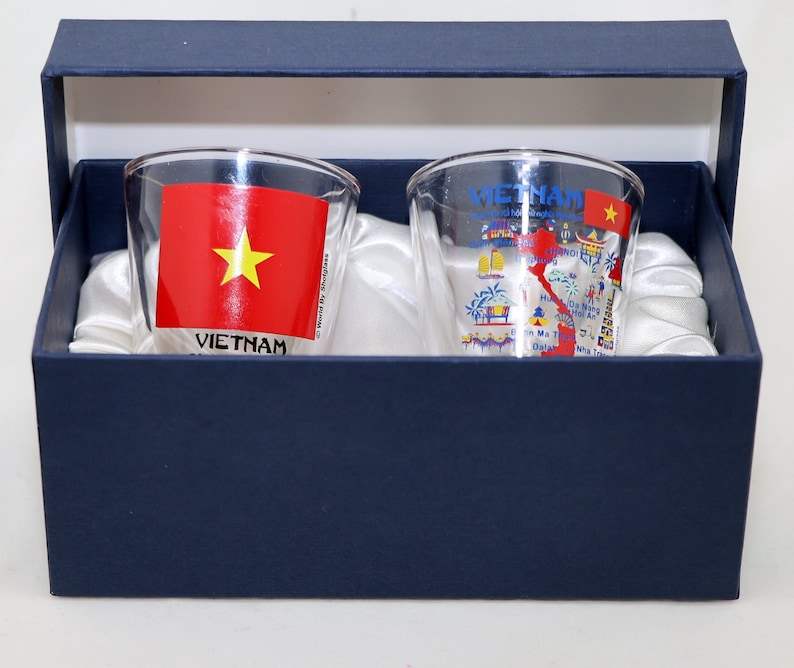 May include: Two clear glass shot glasses with a blue and white design featuring a map of Vietnam and the Vietnamese flag. The glasses are in a blue box with white satin lining.