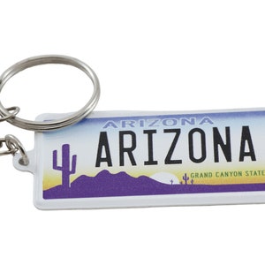 May include: White keychain with a blue and yellow Arizona license plate design. The license plate says "Arizona" and "Grand Canyon State".