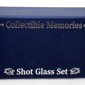 May include: A navy blue box with the text "Collectible Memories" and "Shot Glass Set" printed in silver and white.