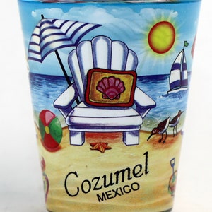 May include: A blue glass shot glass with a beach scene printed on it. The scene includes a beach chair, an umbrella, a sailboat, a beach ball, a seashell, and two birds. The text "Cozumel MEXICO" is printed on the bottom of the glass.