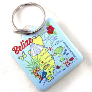 Könnte beinhalten: Ein blauer und gelber Schlüsselanhänger mit einer Karte von Belize. Der Schlüsselanhänger zeigt einen Tukan, einen Schmetterling, eine Schildkröte und eine Maya-Pyramide. Der Text "Belize" ist in roten Buchstaben auf dem Schlüsselanhänger geschrieben.