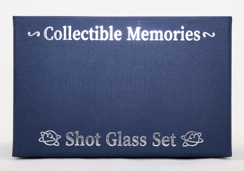 May include: A navy blue box with the text "~Collectible Memories~" and "Shot Glass Set" printed in silver. The box has a textured surface and a silver design on each side.