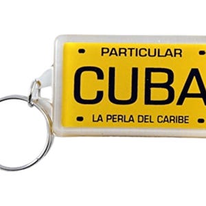 May include: A yellow keychain with a clear plastic cover. The keychain features the word "CUBA" in black letters and the text "LA PERLA DEL CARIBE" in smaller black letters. The keychain also has the word "PARTICULAR" printed on it.