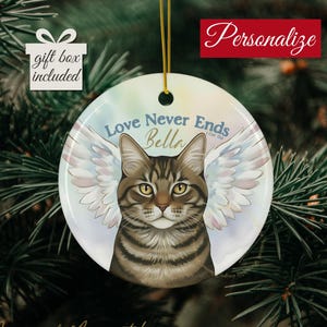May include: A round ceramic ornament featuring a tabby cat with angel wings. The ornament has the text "Love Never Ends Bella" and "Personalize" in red. The words "gift box included" are also visible.