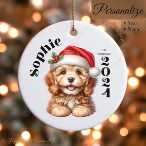 May include: A white ceramic Christmas ornament featuring a cartoon illustration of a golden doodle puppy wearing a Santa hat. The ornament is personalized with the name "Sophie" and the year "2024".