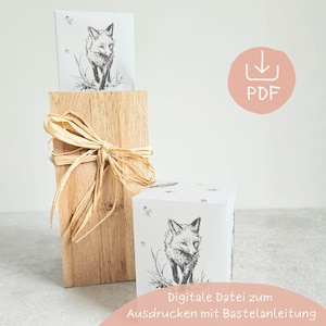 May include: A wooden block with a raffia bow, holding a card with a black and white fox illustration. A white box with a similar fox design is in front. The image includes the text "PDF".