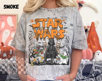 Op de afbeelding: Een grijs T-shirt met een wit tie-dye patroon met een Halloween-thema Star Wars ontwerp. De tekst "STAR WARS" staat in oranje druipende letters met een spinnenwebontwerp. De personages Darth Vader, Yoda, Boba Fett en Stormtroopers zijn afgebeeld als skeletten.