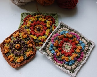 May include: Three crocheted squares featuring colourful floral patterns in shades of orange, brown, green, pink and blue. The squares are made with different coloured yarns and have a textured, raised surface.