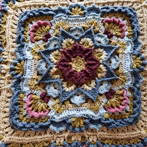 May include: A square, handmade crochet blanket with a central burgundy flower within a blue starburst design. The blanket has a beige background with blue, pink, and gold accents, showcasing intricate stitch work.