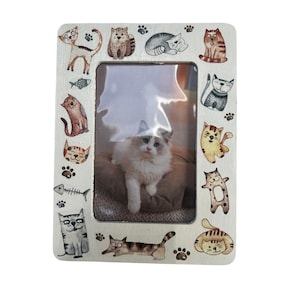 May include: White wooden picture frame with a cat-themed design. The frame has a cutout for a 4x6 inch photo and is decorated with colorful cartoon cats around the border.