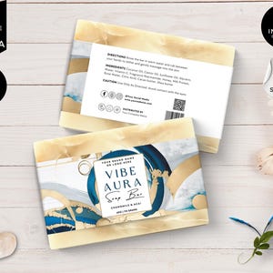 Puede incluir: Una barra de jabón con un diseño abstracto azul, blanco y dorado. El jabón está etiquetado como "Vibe Aura Soap Bar" con el texto "Chamomile & Keai" y "100g" impreso en la etiqueta.