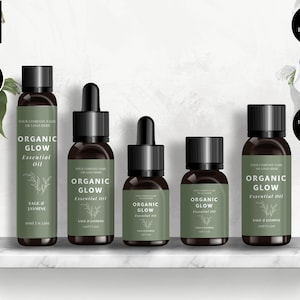 Op de afbeelding: Vijf bruine glazen flessen met druppelaars en etiketten waarop "Organic Glow Essential Oil" in witte tekst staat. De flessen zijn in een rij op een wit marmeren plank geplaatst. De etiketten bevatten ook de tekst "Sage & Jasmine" en "Your Company Name or Logo Here".