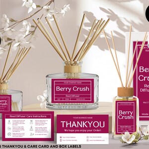 Könnte beinhalten: Produktbild mit Schilf-Diffusoren mit der Aufschrift "Berry Crush". Die Diffusoren befinden sich in Glasflaschen mit Holzaufsätzen und Stäbchen. Das Bild enthält eine Box, Pflegehinweise und eine Dankeskarte. Im Hintergrund weiße Blüten.