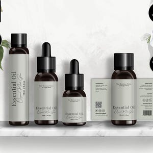 May include: Several essential oil bottles with black lids and labels, displayed on a white shelf. The labels read "Essential Oil" and "Organic Mat G". The background features green leaves. The bottles are in different sizes, from small to larger.