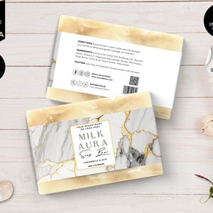 Puede incluir: Una pastilla de jabón de color blanco y dorado con un patrón de mármol y el texto "Milk Aura Soap Bar" y "Chamomile & Acai" impreso en la etiqueta. La pastilla de jabón pesa 4 oz / 113 gramos.
