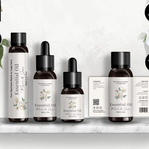 May include: A product mockup showing four essential oil bottles with black caps and white labels. The labels read "Essential Oil" and feature a floral design. The bottles are presented on a white shelf. Sizes are 10ml and 15ml.