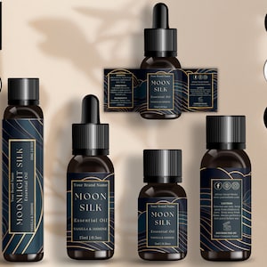 Puede incluir: Cuatro botellas de vidrio negro con detalles dorados y etiquetas. Las botellas están llenas de aceite esencial y tienen goteros. Las etiquetas muestran el texto "Moon Silk" y "Aceite esencial de vainilla y jazmín".