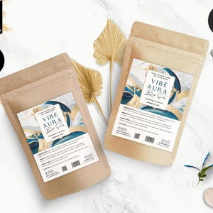 Puede incluir: Dos bolsas de papel marrón con etiquetas para sales de baño. Las etiquetas presentan un diseño abstracto azul y dorado con el texto "VIBE AURA Bath Salts" y "Chamomile & Acai".