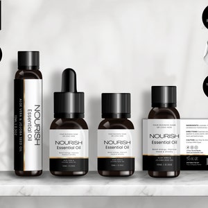 May include: Four small glass bottles with black caps and white labels. The labels have the text "Nourish Essential Oil" and list the ingredients as aloe vera and jojoba seed oil. The bottles are on a white marble shelf.