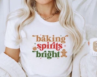 May include: White t-shirt with the text "baking spirits bright" in red, green, and brown letters. The text is surrounded by small stars and a gingerbread man graphic.
