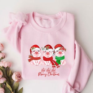 May include: Pink sweatshirt with a Christmas design featuring three pigs wearing Santa hats and scarves. The text "Ho! Ho! Ho! Merry Christmas" is printed below the pigs.