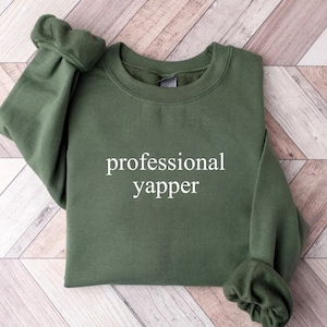 May include: A dark green sweatshirt with the text "professional yapper" printed in white on the front.