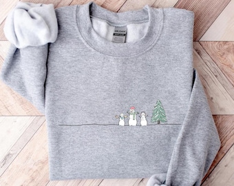 May include: A gray sweatshirt with a simple embroidered design of three snowmen and a Christmas tree. The snowmen are wearing hats and scarves.