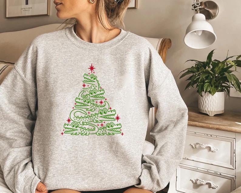 May include: A grey sweatshirt featuring a green alligator Christmas tree design. The tree is made up of alligators stacked on top of each other, with a red star at the top.