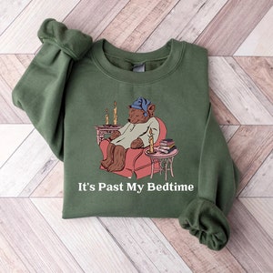 May include: A green sweatshirt with a cartoon bear wearing a nightcap and sitting in a chair with a book and a lit candle. The text "It's Past My Bedtime" is printed below the image.