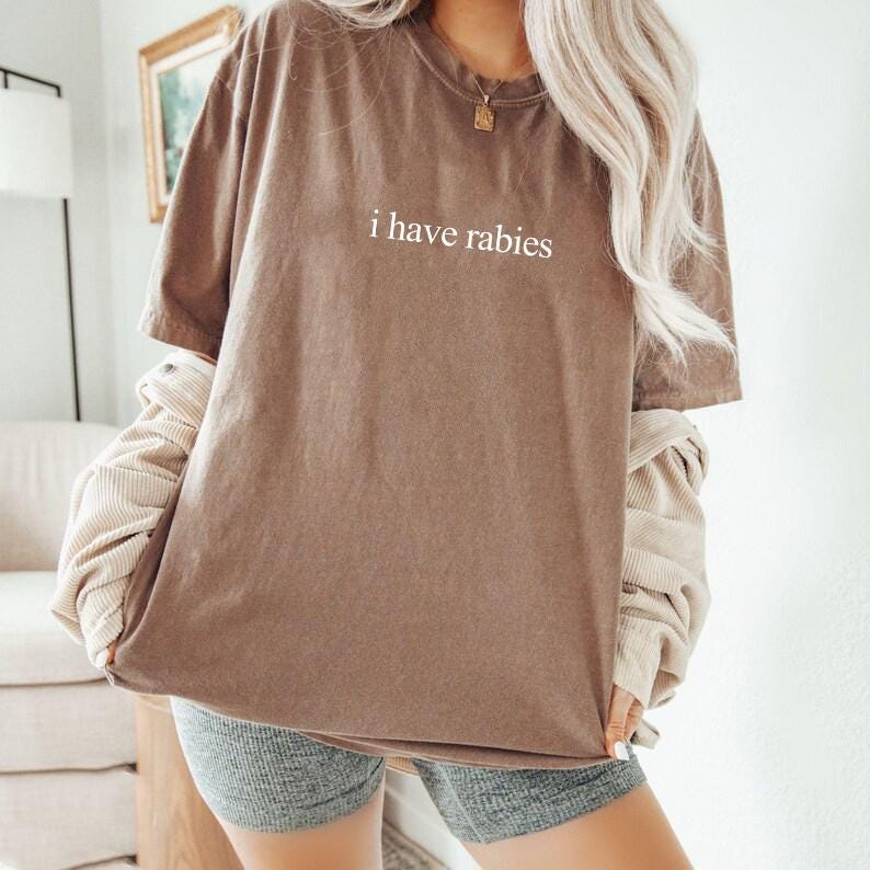 May include: A brown oversized t-shirt with the text "i have rabies" printed in white on the front.