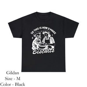 May include: Black t-shirt with a white graphic of a cat and a person making biscuits. The text on the shirt reads "SO THIS IS HOW U MAKE Biscuits."