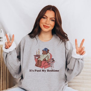 May include: A gray sweatshirt with a cartoon illustration of a bear wearing a nightcap and pajamas, sitting in a chair with a book and a lit candle. The text "It's Past My Bedtime" is printed below the illustration.