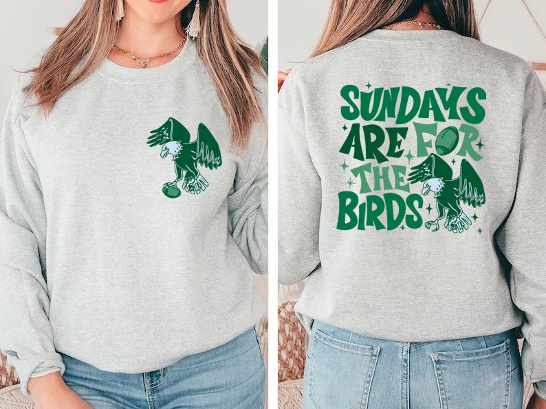 Op de afbeelding: Grijs sweatshirt met een groene adelaar afbeelding op de voorkant en de tekst "Sundays are for the birds" op de achterkant. De adelaar houdt een voetbal vast.