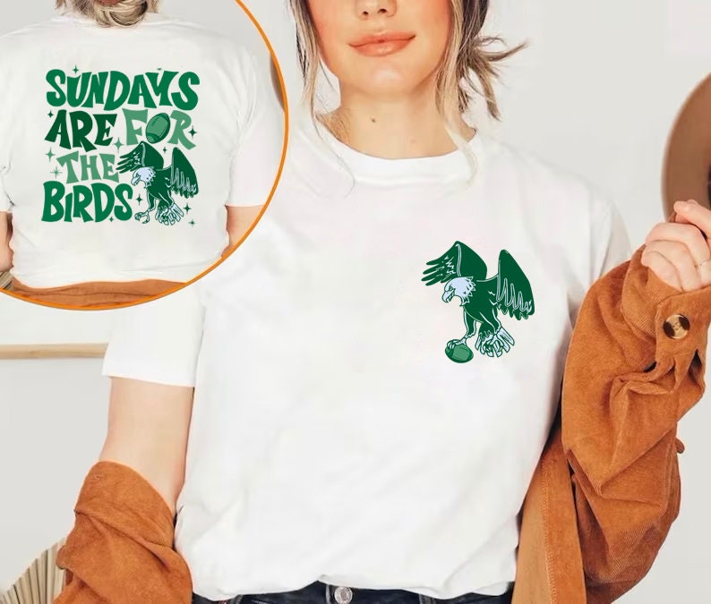 Op de afbeelding: Wit T-shirt met een groene adelaar afbeelding die een voetbal vasthoudt en de tekst "Sundays are for the Birds" op de achterkant.