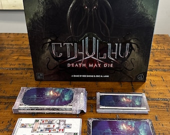 May include: A Cthulhu: Death May Die board game set with a black box featuring a tentacled monster with red eyes. The box is open and shows the game components, including cards, dice, and tokens. The game is set in the Cthulhu Mythos and features a dark and atmospheric theme.