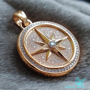 May include: A gold-toned pendant featuring a compass rose with a sparkling diamond center. The compass rose is surrounded by a circle of smaller diamonds.