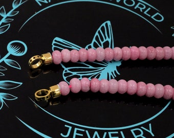 May include: A pink gemstone beaded necklace with gold clasps and black accents. The necklace is on a black background with the words "NATURAL WORLD JEWELRY" in blue.