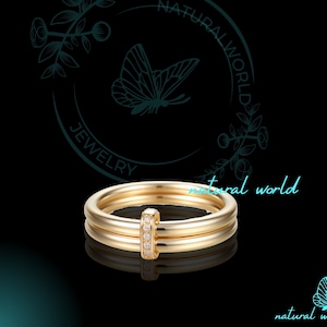 以下が含まれることがあります： 縦のバーに小さなダイヤモンドが並んだ、ゴールドのダブルバンドリング。リングは、蝶と花のデザインが施された黒い背景の上に置かれています。