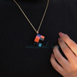 May include: A gold chain necklace with a square pendant. The pendant is made of colorful squares in shades of orange, black, blue, and turquoise.